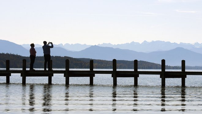 People take a photo of the Alps from a footbridge of the lake Starnberg in front of the Alp mountains near the small Bavarian village of Starnberg, southern Germany, during nice autumn weather with temperatures by 15 degrees on October 17, 2019. (Photo by Christof STACHE / AFP)