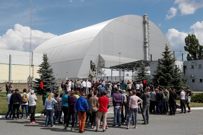 Obiskovalci stojijo pred novim sarkofagom, s katerim so prekrili poškodovani četrti reaktor černobilske jedrske elektrarne. FOTO: Reuters