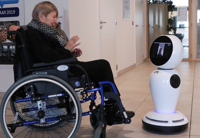 76-letna Belgijka Andree Desmaelle komunicira z domačimi zahvaljujoč robotu, ki ga je belgijsko podjetje ZoraBots brezplačno dalo na razpolago domovom za starejše, ki so na ta način lahko ostali v stiku s svojimi sorodniki zaradi prepovedi obiskov. FOTO: Yves Herman/Reuters
