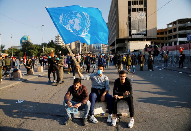 Udeleženec protestov v Iraku z zastavo Združenih narodov. FOTO: Thaier Al-sudani/Reuters