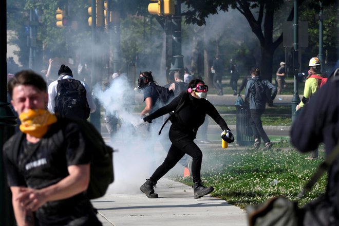 Protestnik v Minneapolisu meče pločevinko s solzivcem nazaj proti policistom. Foto Reuters