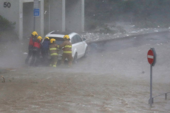 Gasilci pomagajo v poplavah ujetemu vozniku. FOTO: Bobby Yip/Reuters