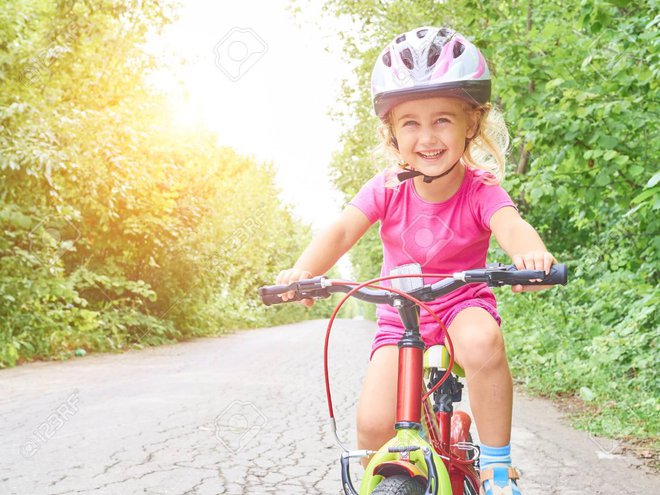 Happy child riding a bike in outdoor. Cute kid in safety helmet biking outdoors. Little girl on a red  bicycle  Healthy preschool children summer activity. 