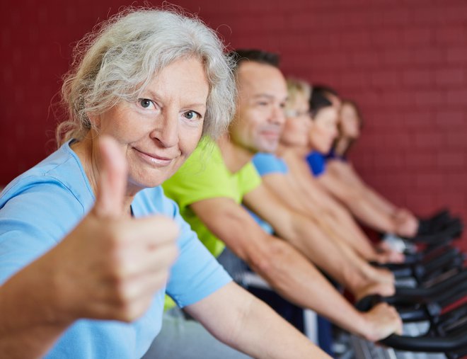 Smiling senior woman holding her thumbs up in spinning class in a fitness center