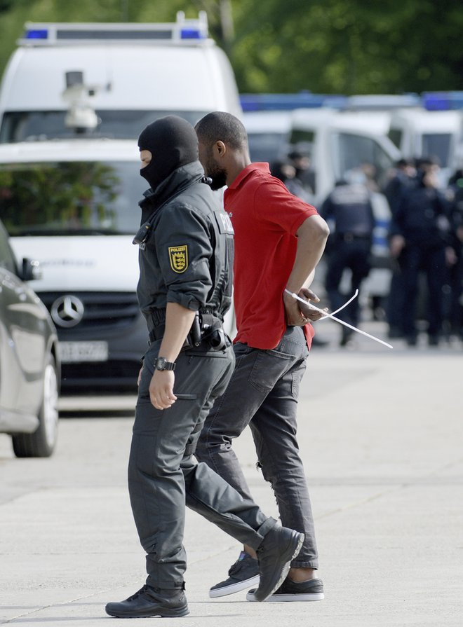 Nemški policist spremlja zavrnjenega prosilca za azil po izbruhu nasilja v begunskem centru v Ellwangnu. FOTO: AP