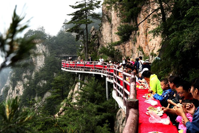 Turisti med banketom ob robu pečine na 2000 metrov visoki gori Laojun na Kitajskem. S tovrstno promocijo želijo domačini privabiti čim več turistov. Foto - Afp