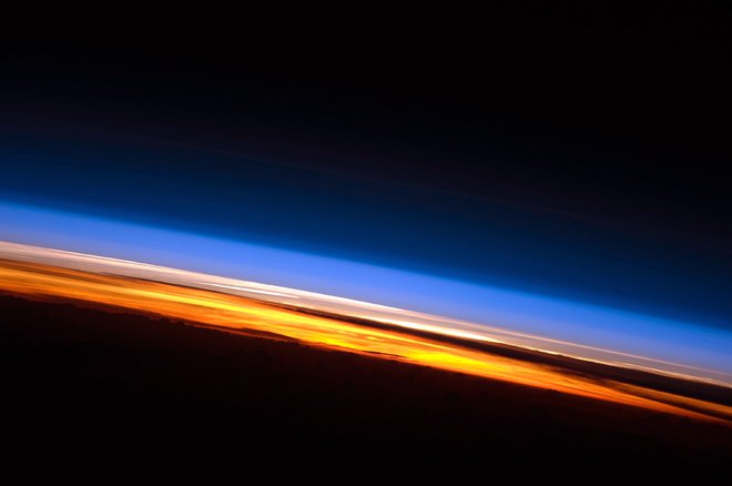 Na tej fotografiji sončnega zahoda, posnetega z Mednarodne vesoljske postaje, so jasno vidne tri plasti atmosfere: troposfera se sveti oranžno, stratosfera, kjer se najaha ozon, je roza, višje plasti so modrikaste. FOTO: Nasa
