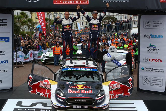 Sebastien Ogier in njegov sovoznik Julien Ingrassia sta se takole na strehi svojega forda veselila četrte letošnje zmage v svetovnem prvenstvu. FOTO: Geoff Caddick/AFP