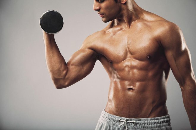 Cropped image of young muscular man doing heavy dumbbell exercise for biceps. Man working out with dumbbells on grey background. Fitness and workout concept.