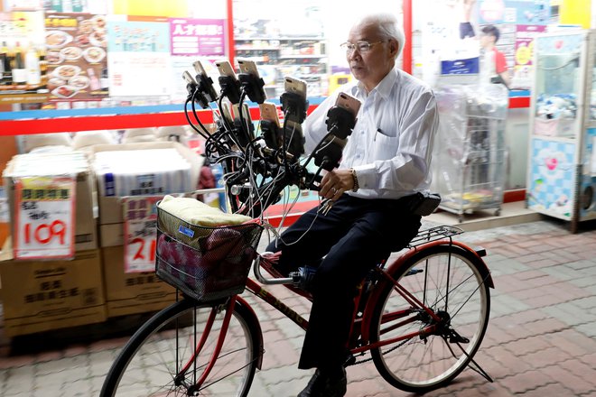 Tajvanski 70-letnik Chen San-yuan, znan kot dedek Pokemon, vozi svoje kolo po ulici v Tajpeju in istočasno igra igrico Pokemon kar na 15. pametnih telefonih.&nbsp;Foto Tyrone Siu Reuters