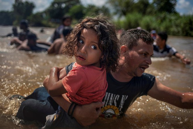Luis Acosta iz Hondurasa nosi 5-letnega Anhela Jezusa med prečkanjem reke Suchiate na meji med Gvatemalo in Mehiko, skupaj z ostalo karavano priseljencev iz Srednje Amerike na poti v ZDA. Foto Adrees Latif Reuters