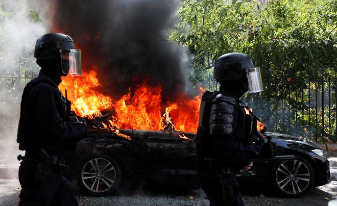 Francoski policisti ob zažganem avtomobilu med današnjim protestom rumenih jopičev v Parizu. FOTO: Gonzalo Fuentes/Reuters