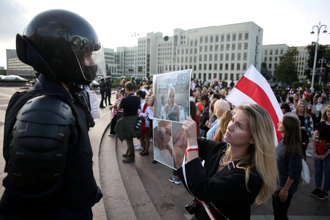 Protestniki zahtevajo razveljavitev volitev in odstop predsednika. Protestnica na sliki policistu kaže fotografijo protetsnice, ki so jo poškodovale varnostne sile. FOTO: izroček Via Reuters