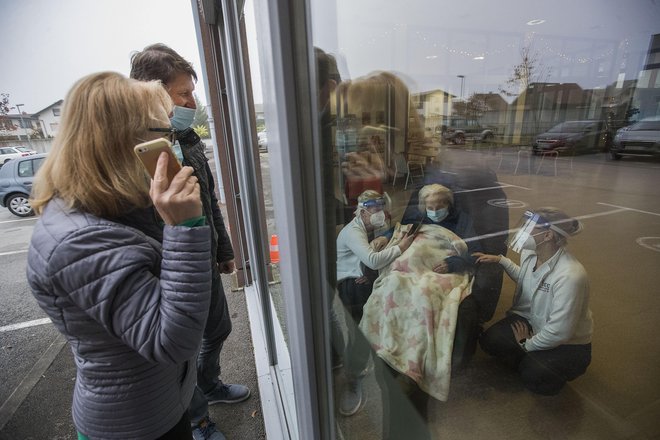 Hčerka je materi v domu upokojencev za njen 91. rojstni dan čestitala po mobilnem telefonu skozi vrata. FOTO: Leon Vidic/Delo