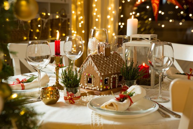 Medena hiška sredi belo pogrnjene mi&shy;ze z zeleno-rdečimi dodatki bo skupaj s toplimi lučkami in prižganimi svečami ustvarila popolno božično-novoletno vzdušje. FOTO: Shutterstock