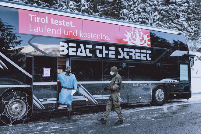 Avstrijski vojaki stojijo ob avtobusu, v katerem lahko test za covid-19 opravijo potniki, ki prihajajo s Tirolske in nimajo s sabo svežega dokazila o neobolelosti. FOTO: AFP