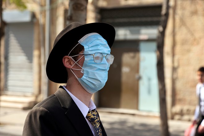 Med praznovanjem veselega festivala Purim na ulici v Jeruzalemu ultra pravoslavni Jud nosi tri maske eno čez drugo. FOTO: Ronen Zvulun/Reuters