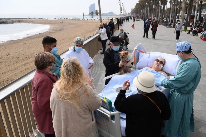 Prijatelji, sosedje in zdravstveno osebje obkrožajo 72-letno bolnico s COVID-19 Marto Pascual, ko je na plaži Barceloneta, ki se nahaja v neposredni bližini bolnice del Mar v Barceloni dobila svež zrak. FOTO: Lluis Gene/Afp