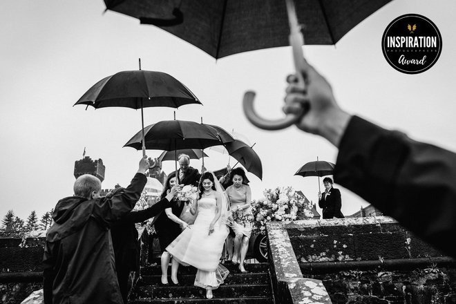 Kljub dežju prihaja nevesta nasmejana na poročni obred (Ashford Castle, Irska).