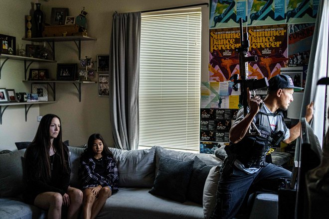Oborožen član skupine Freedom Fighters (MNFF) iz Minnesote gleda skozi okno svojega doma v Minneapolisu, na kavču pa sedita partnerica in hčerka. Samoobrambna skupina, ustanovljena po smrti Georgea Floyda, se opisuje kot most med policijo in afriško-ameriško skupnostjo. FOTO: Kerem Yucel/Afp