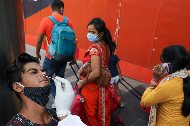 Indijec reagira, ko zdravstveni delavec odvzema vzorec brisa med širjenjem koronavirusa na železniški postaji v New Delhiju. FOTO: Anushree Fadnavis/Reuters