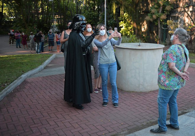 Tako kot je čakajoče na cepljenje proti covidu-19 v Riu de Janeiru nedavno zabaval filmski junak Darth Vader, čakajoče na cepivo v Sloveniji te dni zabava razprava o prav tako črnem karantanskem panterju. FOTO: Carl De Souza Afp