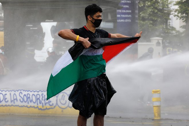 Protestnik v Parizu drži palestinsko zastavo, medtem, ko ga &quot;obstrejujejo&quot; z vodnim topom. FOTO:&nbsp;Geoffroy Van Der Hasselt/ AFP