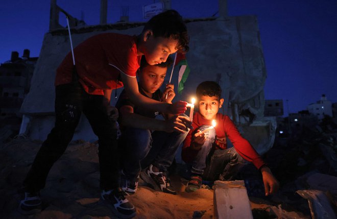 Palestinski otroci prižigajo sveče med shodom pred ruševinami hiš, ki so jih uničili izraelski zračni napadi v Gazi. FOTO: Mohammed Abed/Afp