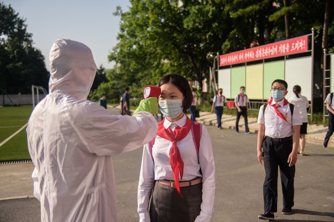 Učenki pred vstopom v srednjo šolo v Pjongjangu merijo temperaturo. FOTO:  Kim Won Jin/AFP