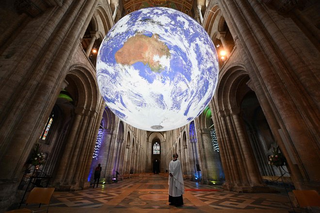 Član duhovščine si ogleduje instalacijo britanskega umetnika Luke Jerrama, ki jo je poimenoval Gaia. 7-metrska replika planeta Zemlja je na ogled v katedrali, ki se nahaja v angleškem mestu Ely. FOTO: Oli Scarff/Afp<br />
&nbsp;