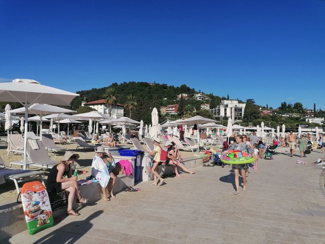 Vrvež na osrednji portoroški plaži, beli senčniki z ležalniki so namenjeni gostom hotela Kempinski Palace. FOTO: Nataša Čepar/Delo