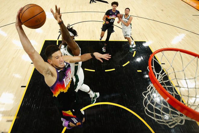 Devin Booker (z žogo) se pripravlja na zabijanje ob Jrueju Holidayu. FOTO: Christian Petersen/AFP