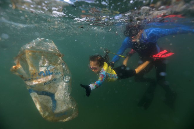 4-letna Nina Gomes, ki jo je komunalno podjetje COMLURB iz Ria de Janeira imenovalo za najmlajšega zelenega agenta, zbira smeti v morju na plaži Praia Vermelha v Riu de Janeiru, ob spremstvu očeta Ricarda Gomesa, morskega biologa in direktorja nevladne organizacije Instituto Mar Urbano. FOTO: Pilar Olivares/Reuters