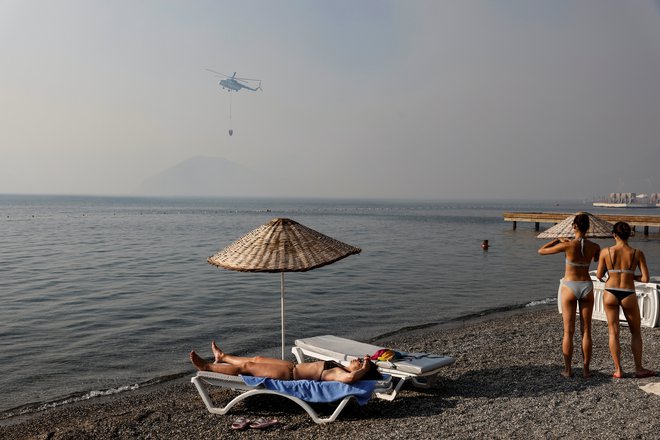 Turisti opazujejo helikopter, ki zajema vodo za gašenje požara blizu Marmare. FOTO: Umit Bektas/Reuters