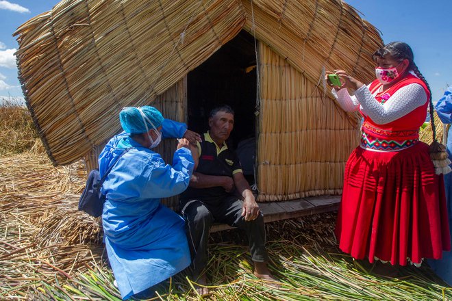 Delavec perujskega ministrstva za zdravje cepi lokalnega prebivalca v okviru programa za imunizacijo ranljivega prebivalstva na plavajočem otoku Uros na jezeru Titicaca, v Peruju. Več kot 1700 članov domorodnega ljudstva Uros živi na približno 140 umetno narejenih plavajočih otokih iz trsja. FOTO: Carlos Mamani/Afp<br />
<br />
&nbsp;