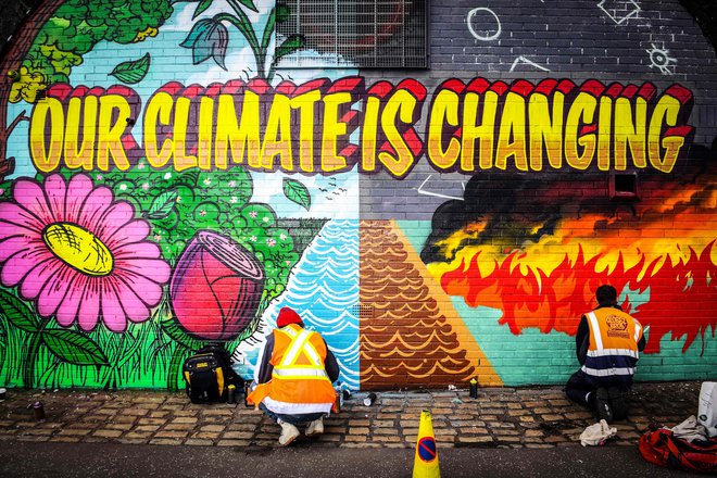 Ulična umetnika barvata zid, ki stoji nasproti prizorišča podnebne konference Združenih narodov v Glasgowu. FOTO: Andy Buchanan/AFP
