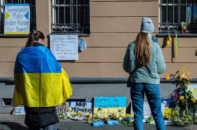 Ženska, zavita v ukrajinsko zastavo, gleda improvizirani spomenik pred ukrajinskim veleposlaništvom v Berlinu. FOTO: John Macdougall/AFP
