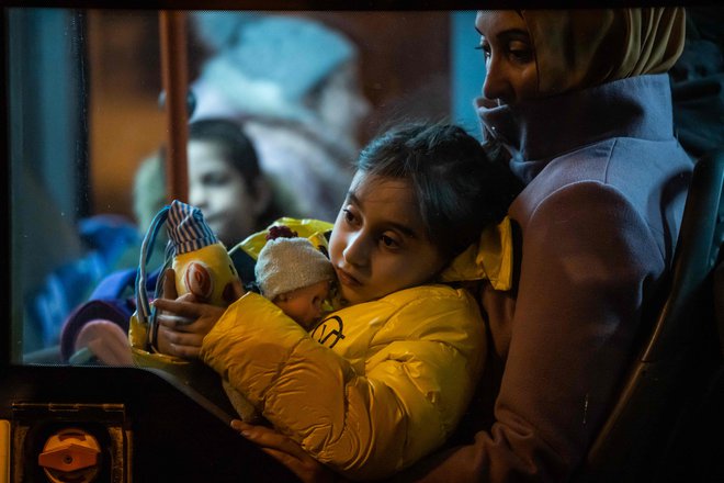 Mladi begunec, ki prihaja iz Ukrajine, sedi v naročju ženske v avtobusu po prihodu na severno železniško postajo v Bukarešti. FOTO: Mihai Barbu/AFP
