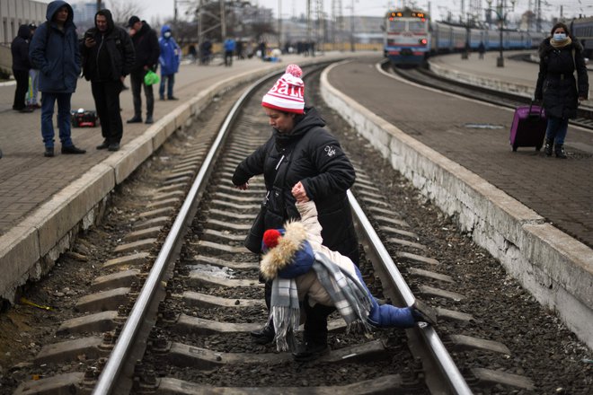Mati pomaga otroku čez tire na osrednji železniški postaji v Kijevu. Svet za človekove pravice pri Združenih narodih je danes izglasoval preiskavo kršenja človekovih pravic po ruski invaziji v Ukrajini. Slednjo je zapustilo že več kot 1,2 milijona beguncev. FOTO:&nbsp;Daniel Leal/AFP
