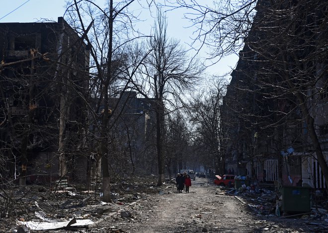 Lokalni prebivalci hodijo v bližini stanovanjskih zgradb, ki so bile poškodovane v mestu Mariupol. FOTO: Stringer/Reuters
