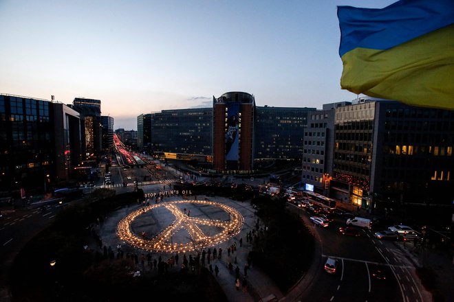 Člani organizacije Avaaz, demonstranti in ukrajinski aktivisti stojijo ob znaku miru med budnostjo za Ukrajino v bližini sedeža Evropske unije v Bruslju. Demonstranti pozivajo voditelje EU, naj uvedejo popolno prepoved uvoza ruskih goriv. FOTO: Valeria Mongelli/AFP
