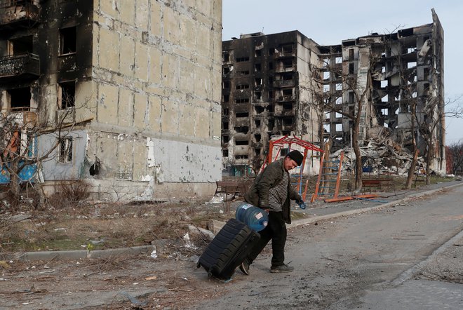 Lokalni prebivalec gre s kovčkom mimo stanovanjskih zgradb, uničenih med ukrajinsko-ruskim konfliktom v poraženem južnem pristaniškem mestu Mariupolj. FOTO: Alexander Ermochenko/Reuters
