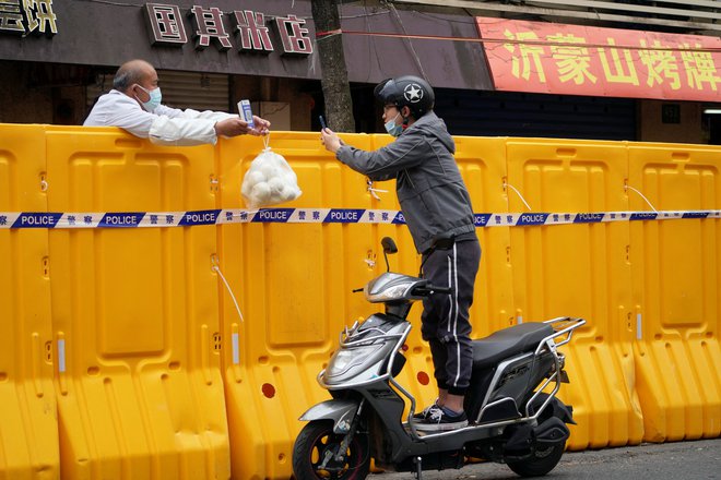 Moški na skuterju skenira QR kodo ob dostavi hrane na zaprtem območju v Šanghaju po ponovnem izbruhu koronavirusa. Zaradi najhujšega izbruha novega koronavirusa na Kitajskem doslej je moral pred 10. dnevi zapreti svoja vrata Disneyland v Šanghaju, potem ko so v več večmilijonskih mestih že odredili stroga zaprtja. Oblasti v Hongkongu so medtem kljub valu okužb za april napovedale omilitve zajezitvenih ukrepov.Foto: Aly Song/Reuters
