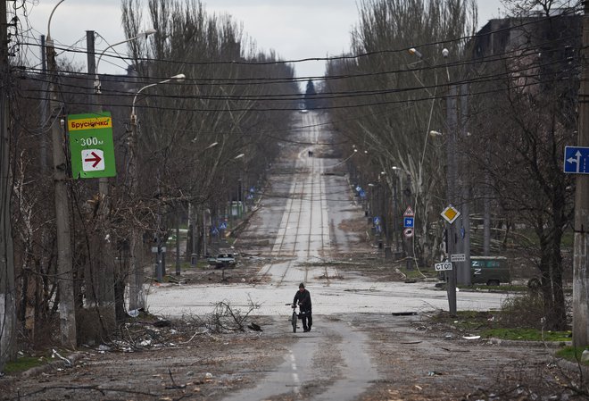 Prebivalec hodi ob kolesu na ulicah Mariupola. FOTO: Stringer/Reuters
