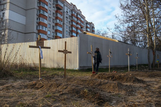 Moški stoji ob grobovih s trupli civilistov, ki so jih po navedbah lokalnih prebivalcev ubili ruski vojaki v Buči. FOTO: Stringer/Reuters
