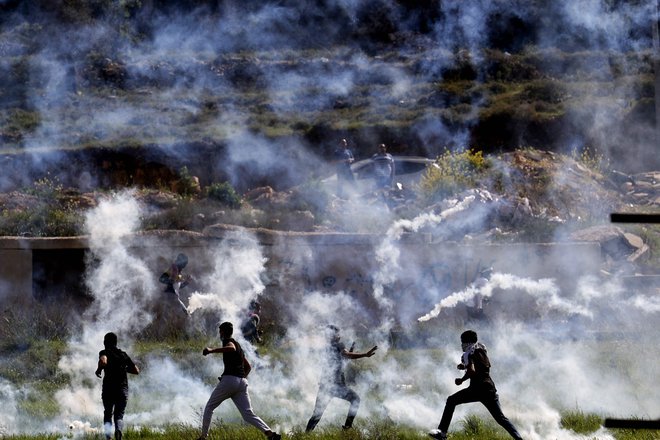 Palestinci se skrivajo pred solzivcem med spopadi z izraelskimi varnostnimi silami na severnem vhodu v Ramalo v bližini izraelske naselbine Beit El, na okupiranem Zahodnem bregu. Foto: Abbas Momani/Afp
