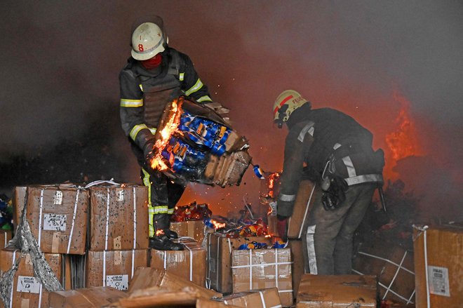 Gasilci rešujejo škatle, medtem ko skušajo pogasiti požar po tem, ko je raketa zadela skladišče na obrobju Harkova. Foto: Sergej Bobok/Afp
