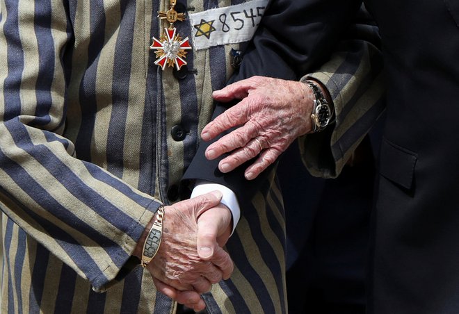 Poljski predsednik Andrzej Duda in Edward Mosberg, ki je&nbsp;preživel holokavst, se držita za roke pred &raquo;zidom smrti&laquo;. Gre za vsakoletni mednarodni Pohod živih po območju nekdanjega taborišča smrti Auschwitz v Oswiecimu na Poljskem. Foto: Kacper Pempel/Reuters
