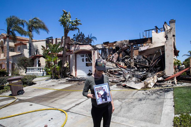 Lynn Morey stoji pred svojim požganim domom in drži portret nje in njenega moža Keitha Moreyja, ki ga je gasilec nezavestnega našel po požaru v Laguni Niguel v Kaliforniji. Nenaden in silovit požar, ki je v nekaj minutah zajel luksuzno enklavo v Kaliforniji in uničil več milijonov dolarjev vredne hiše, sta poslabšala veter in velikost nepremičnin. Požar, ki je izbruhnil 11. maja, se je hitro širil in zajel skupnost Laguna Niguel v bližini Los Angelesa. Okoli 1 000 domov je bilo evakuiranih, saj se je požar razširil na 80 hektarjev , uničil in poškodoval pa je okoli 30 nepremičnin. Foto: Apu Gomes/Afp
