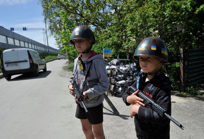 Ukrajinski otroci se igrajo borce teritorialne obrambe na lažni kontrolni točki v vasi Stojanka v okolici Kijeva. Foto: Sergej Čuzavkov/Afp
